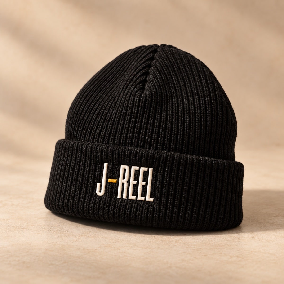 Original concept black ribbed beanie with ivory J-Reel lettering and a gold hyphen